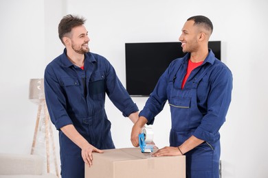 Male movers packing box with adhesive tape in house