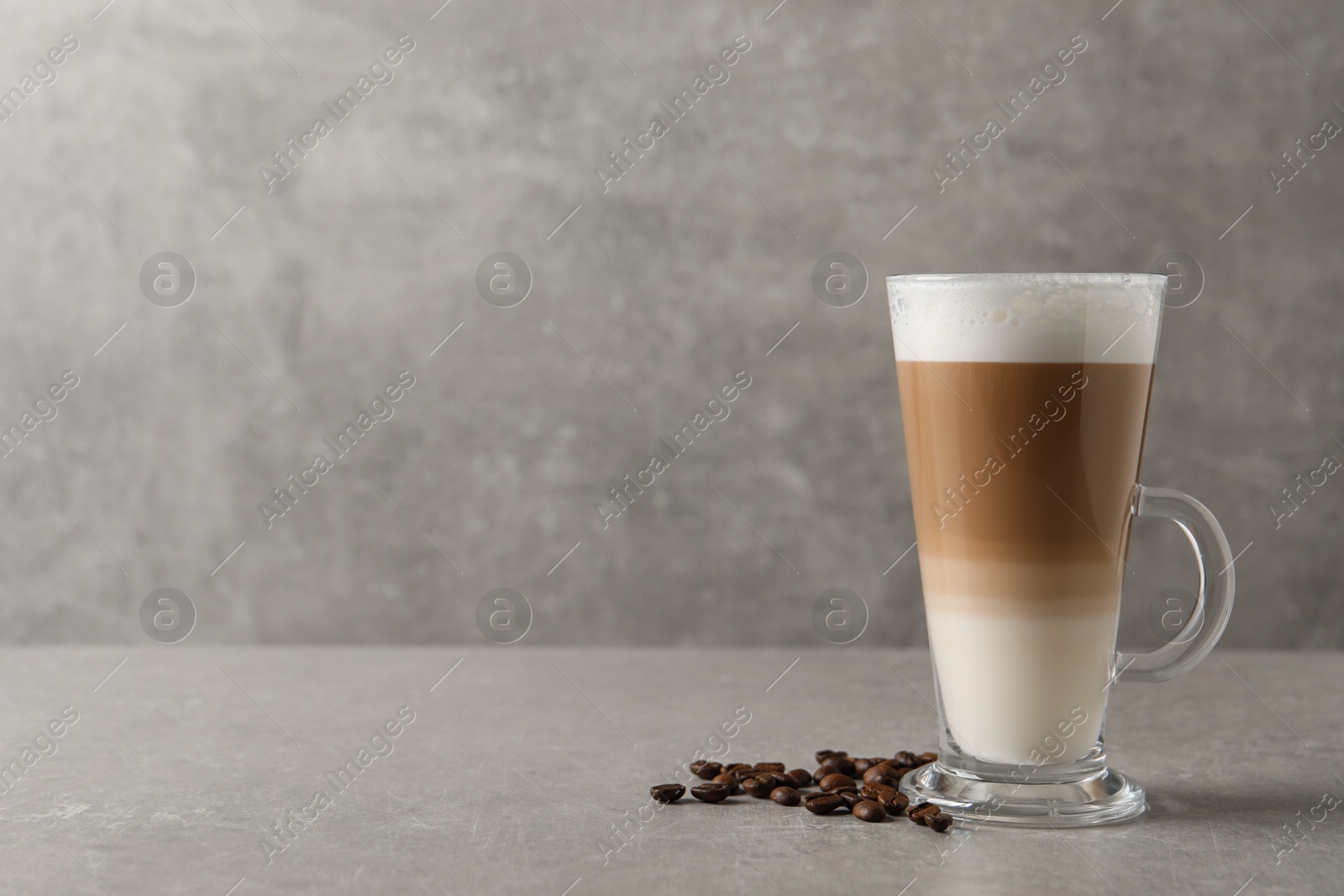 Photo of Glass cup of delicious layered coffee and beans on grey table, space for text