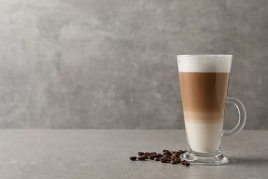 Glass cup of delicious layered coffee and beans on grey table, space for text