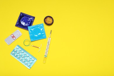 Photo of Contraceptive pills, condoms, intrauterine device and thermometer on yellow background, flat lay and space for text. Different birth control methods