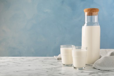 Photo of Carafe and glass of fresh milk on white marble table, space for text