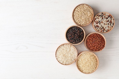 Flat lay composition with brown and other types of rice in bowls on white wooden background. Space for text