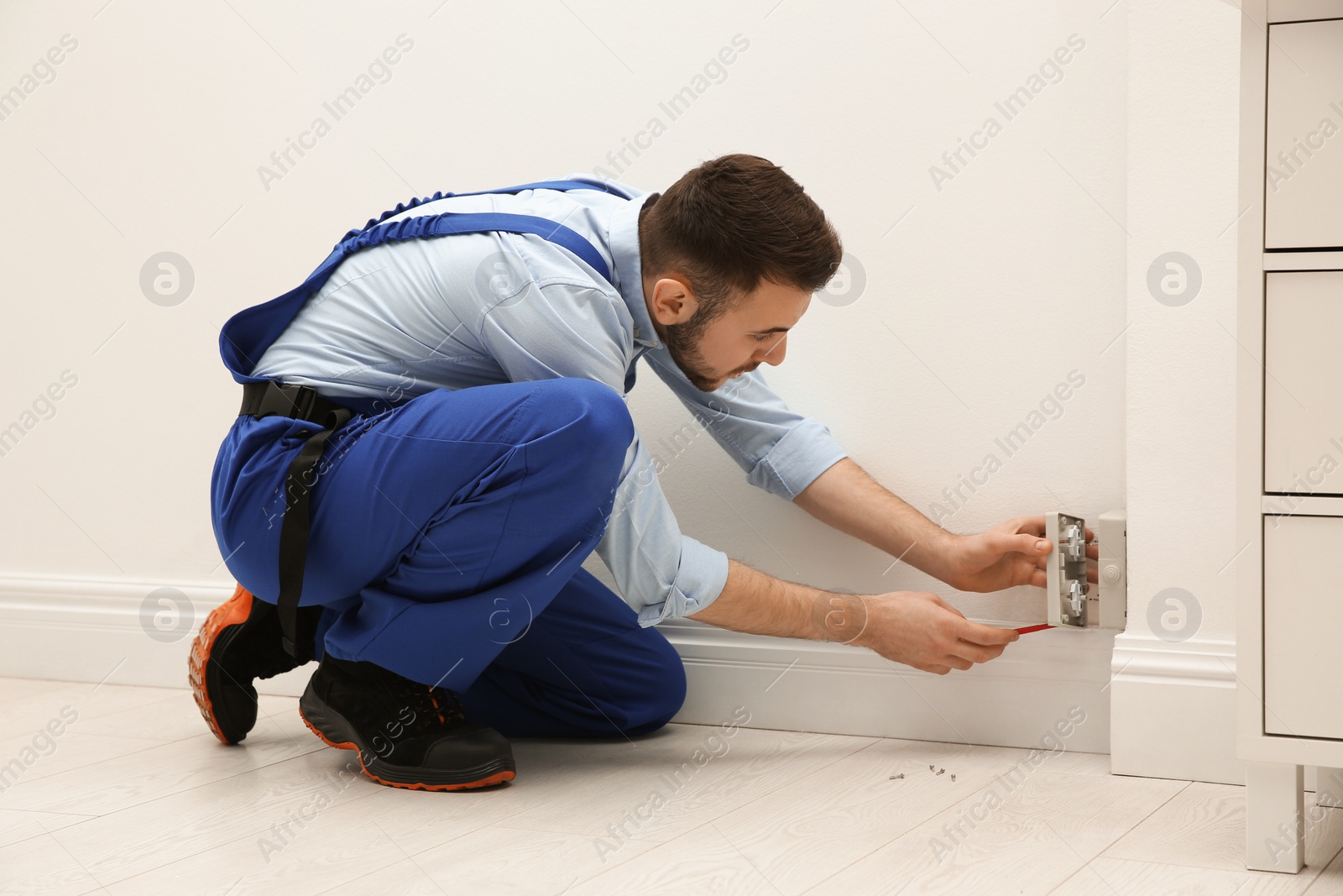 Photo of Electrician with screwdriver repairing power socket indoors