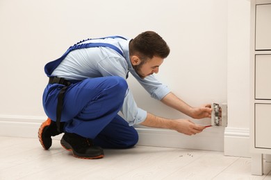 Electrician with screwdriver repairing power socket indoors