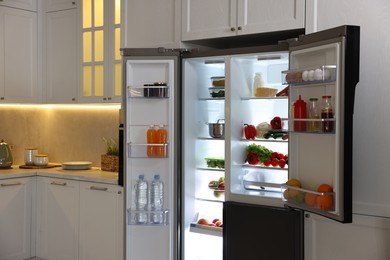 Open refrigerator full of different products in kitchen