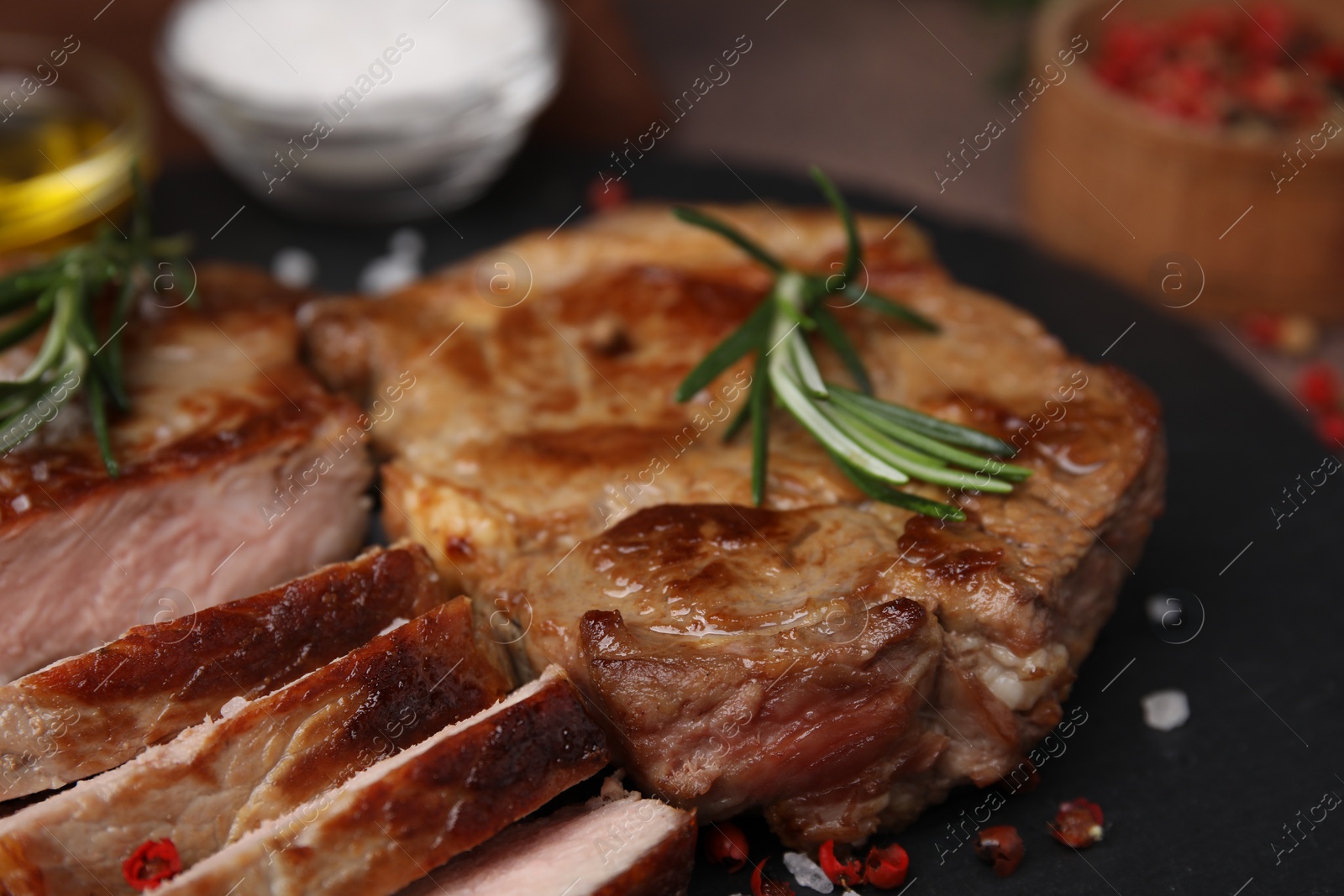 Photo of Pieces of delicious fried meat with rosemary and spices on slate plate, closeup