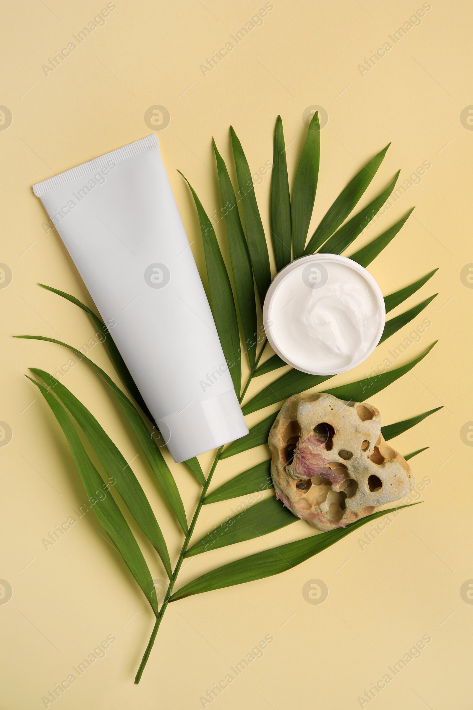 Photo of Cosmetic products, palm leaf and beautiful stone on beige background, flat lay