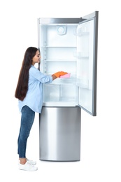 Young woman cleaning refrigerator with rag on white background