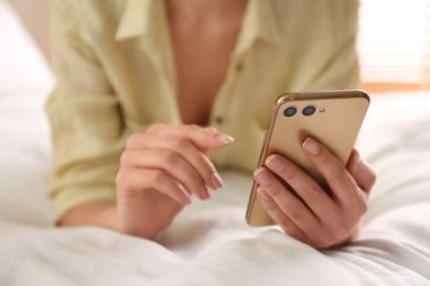 Photo of Young woman using modern smartphone on bed at home, closeup