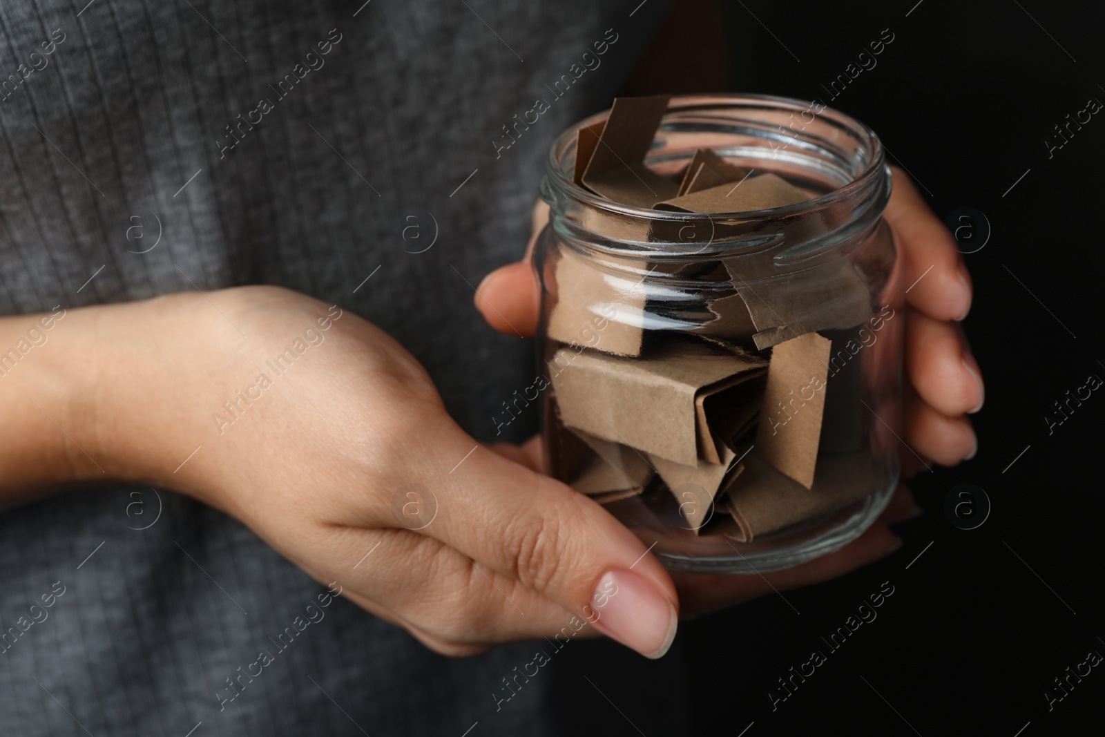 Photo of Woman holding glass jar with paper pieces, closeup on hands