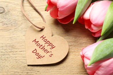 Image of Happy Mother's Day. Heart shaped greeting label and beautiful flowers on wooden table
