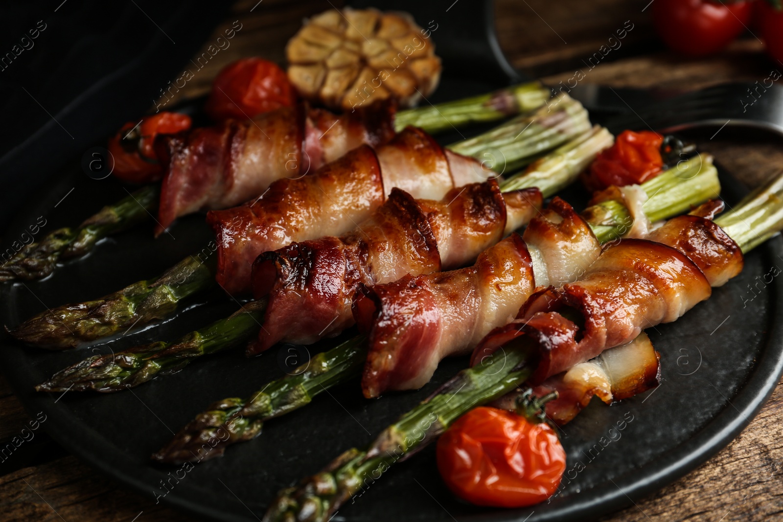 Photo of Oven baked asparagus wrapped with bacon on black slate board, closeup