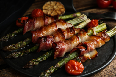 Photo of Oven baked asparagus wrapped with bacon on black slate board, closeup