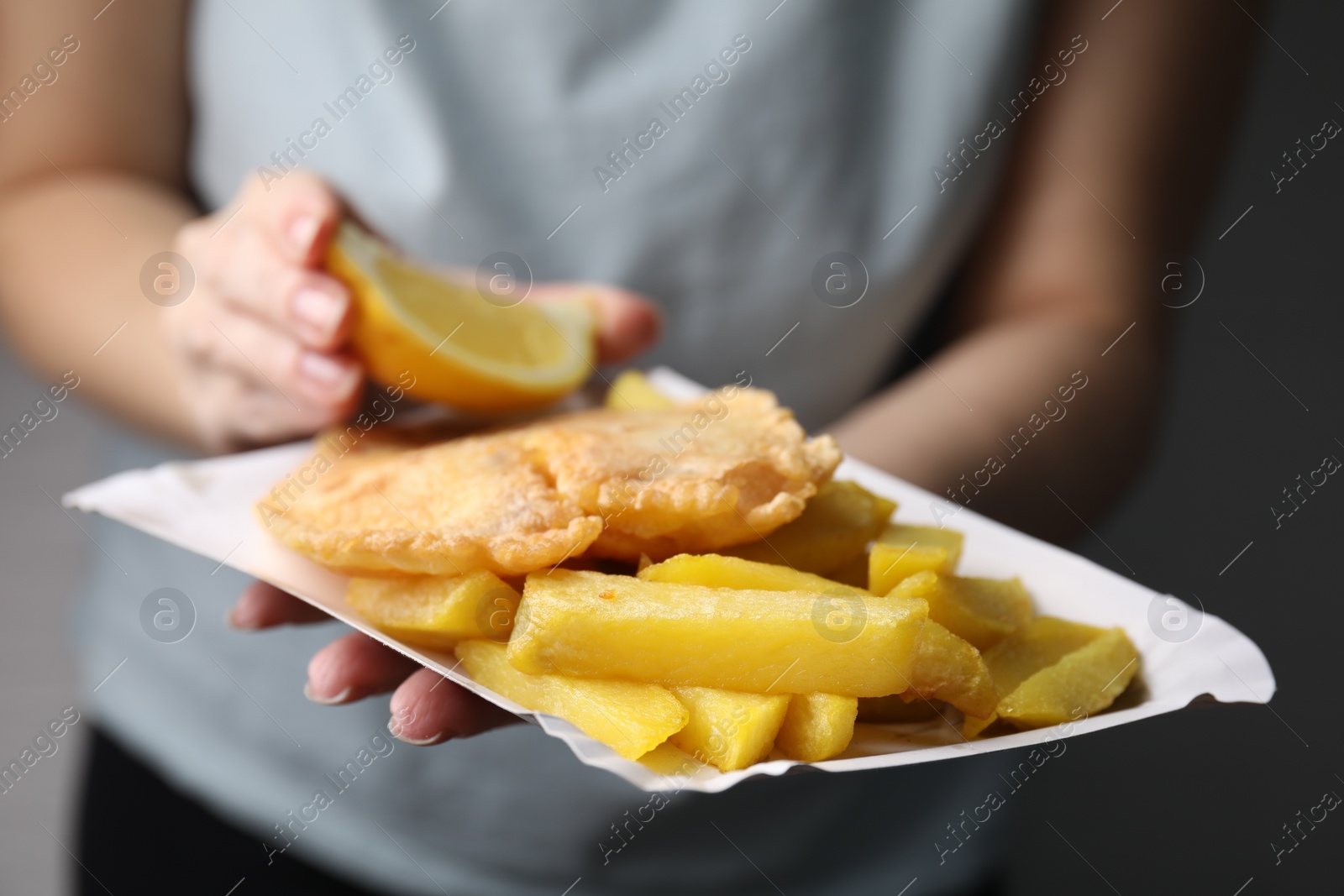 Photo of Woman adding lemon to delicious fish and chips on gray background, closeup