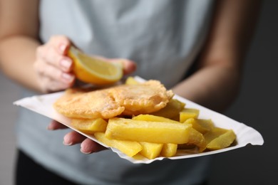 Photo of Woman adding lemon to delicious fish and chips on gray background, closeup