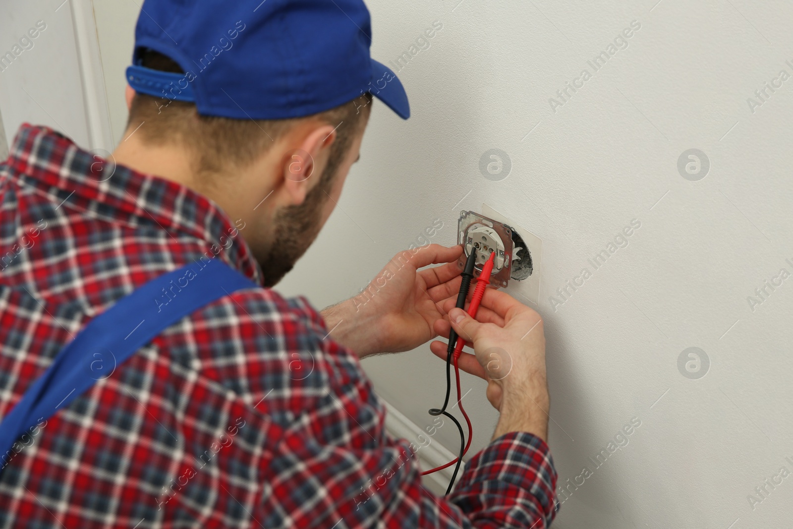 Photo of Professional electrician with tester checking voltage indoors