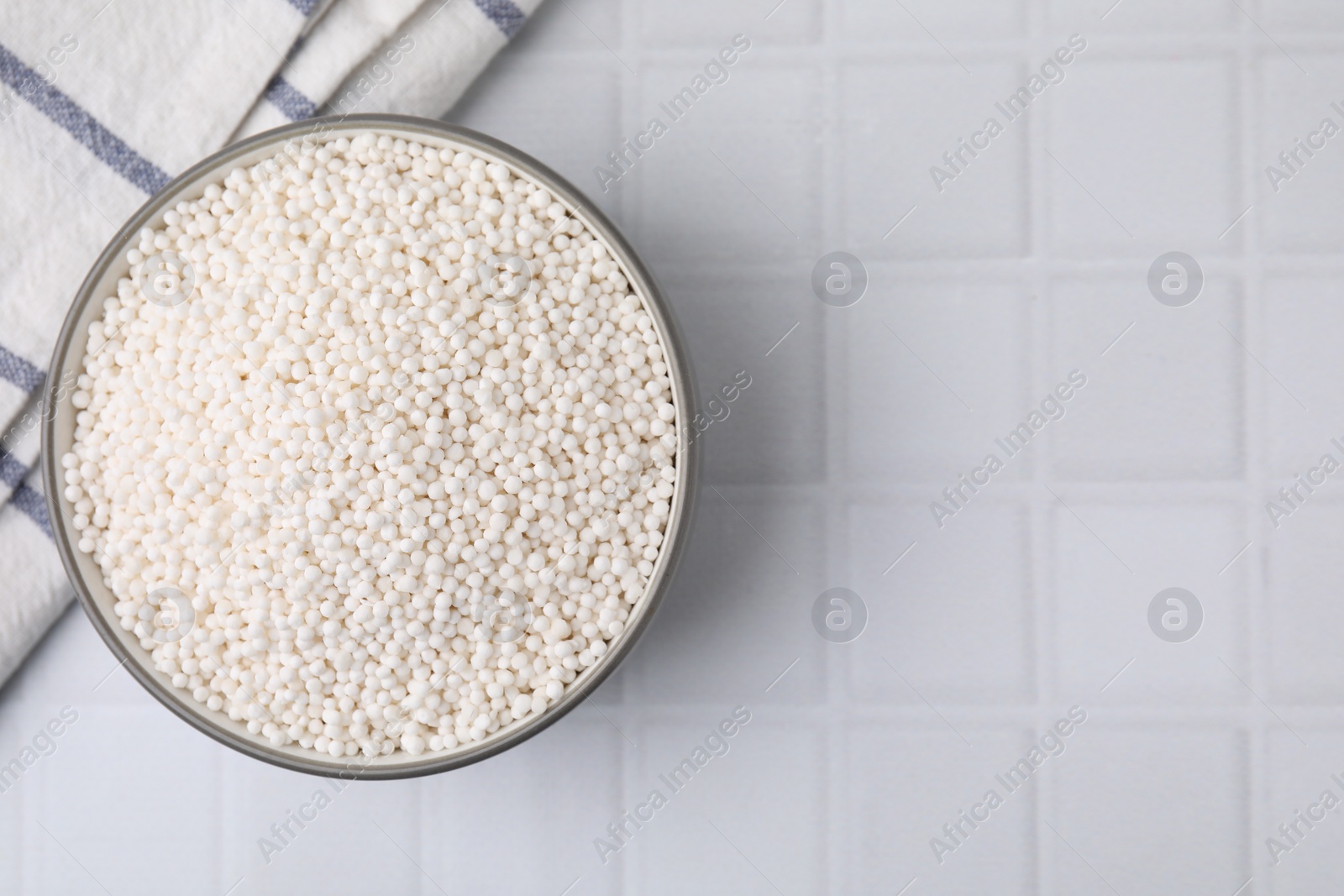Photo of Tapioca pearls in bowl and towel on white tiled table, top view. Space for text