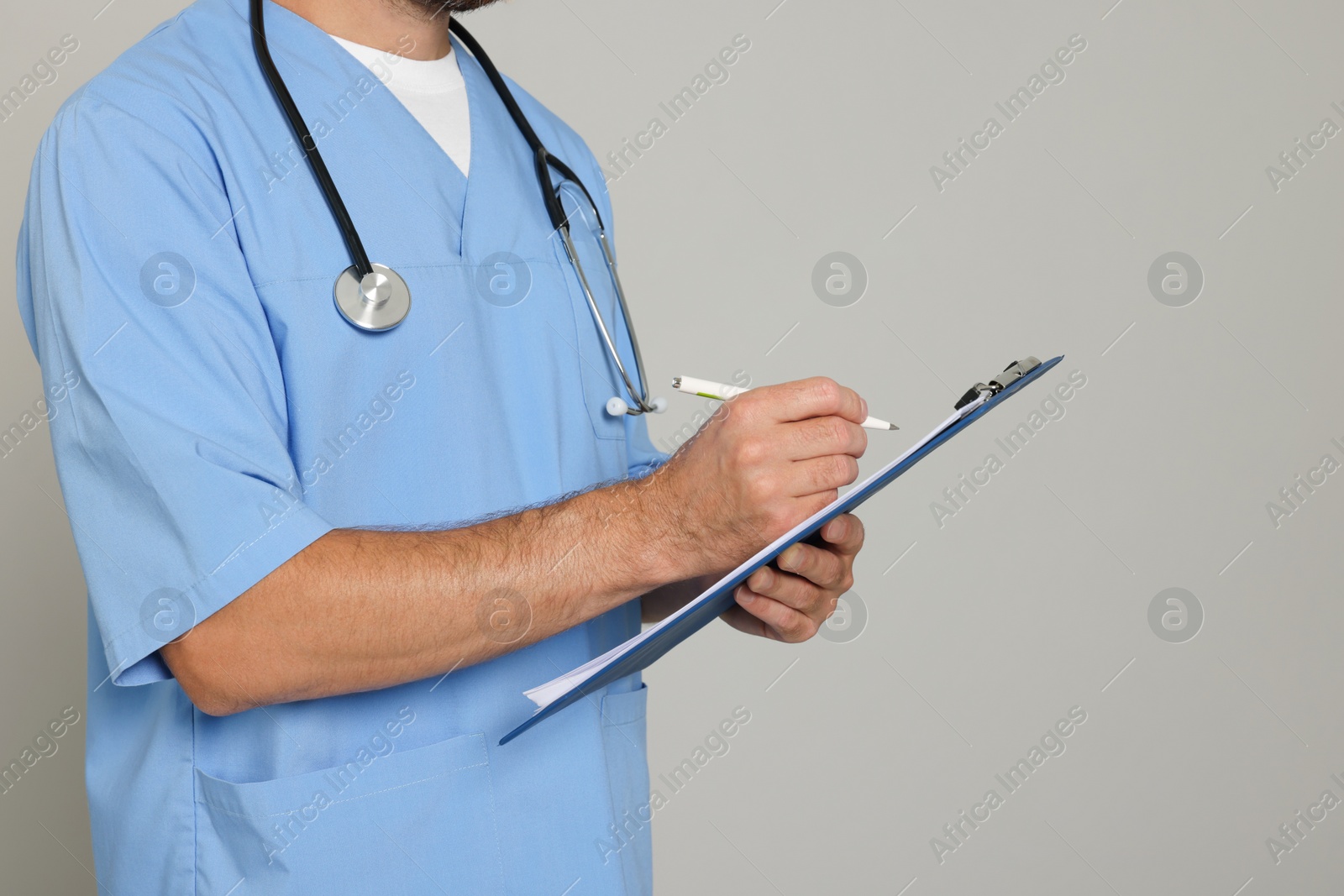 Photo of Doctor with stethoscope and clipboard on light grey background, closeup