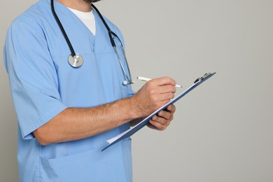 Doctor with stethoscope and clipboard on light grey background, closeup