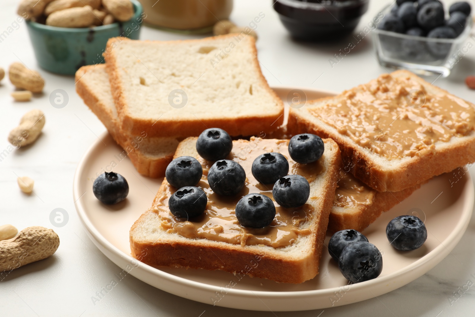 Photo of Delicious toasts with peanut butter and blueberries on white table, closeup