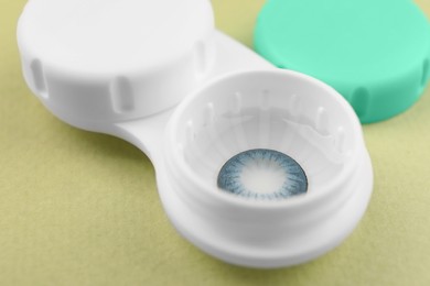 Photo of Case with blue contact lenses on light green background, closeup