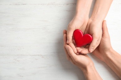 People holding red heart on wooden background, top view with space for text. Cardiology concept