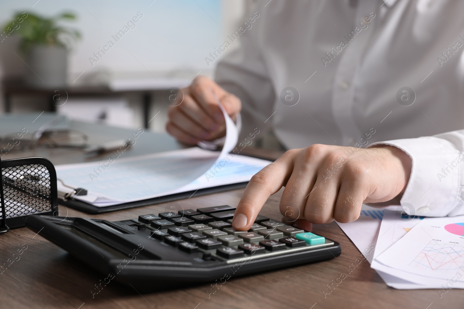 Photo of Man using calculator at wooden table indoors, closeup