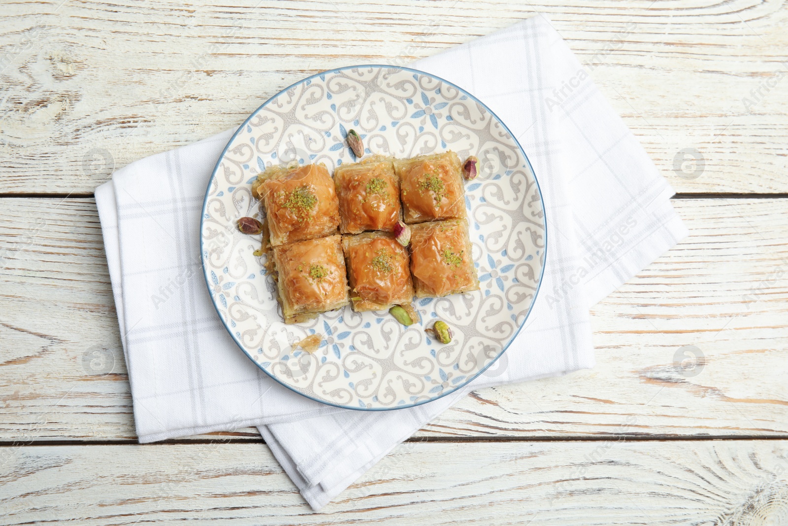 Photo of Delicious baklava with pistachio nuts and napkin on white wooden table, top view