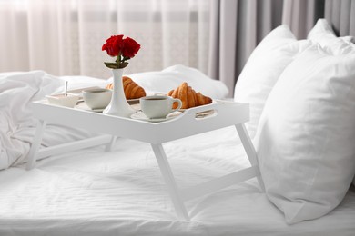 Photo of Tray with tasty breakfast and flowers on bed at home