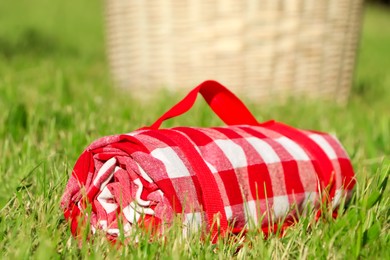 Photo of Rolled checkered picnic tablecloth on green grass, closeup