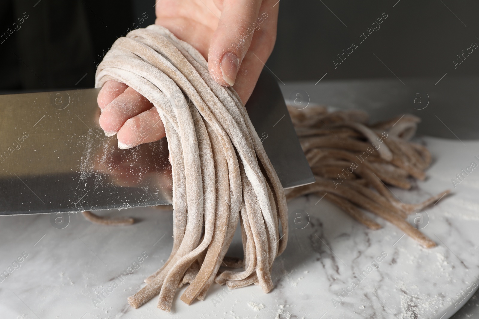 Photo of Woman making soba (buckwheat noodles) at white marble table, closeup