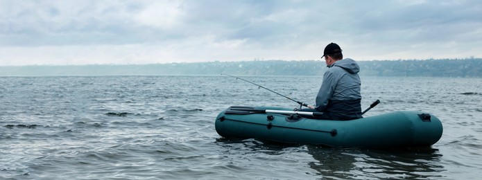 Image of Man fishing with rod from inflatable rubber boat on river, space for text. Banner design