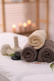 Spa stones, rolled towels and herbal bags on massage table indoors