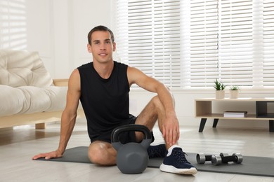 Photo of Handsome man with kettlebell on floor at home