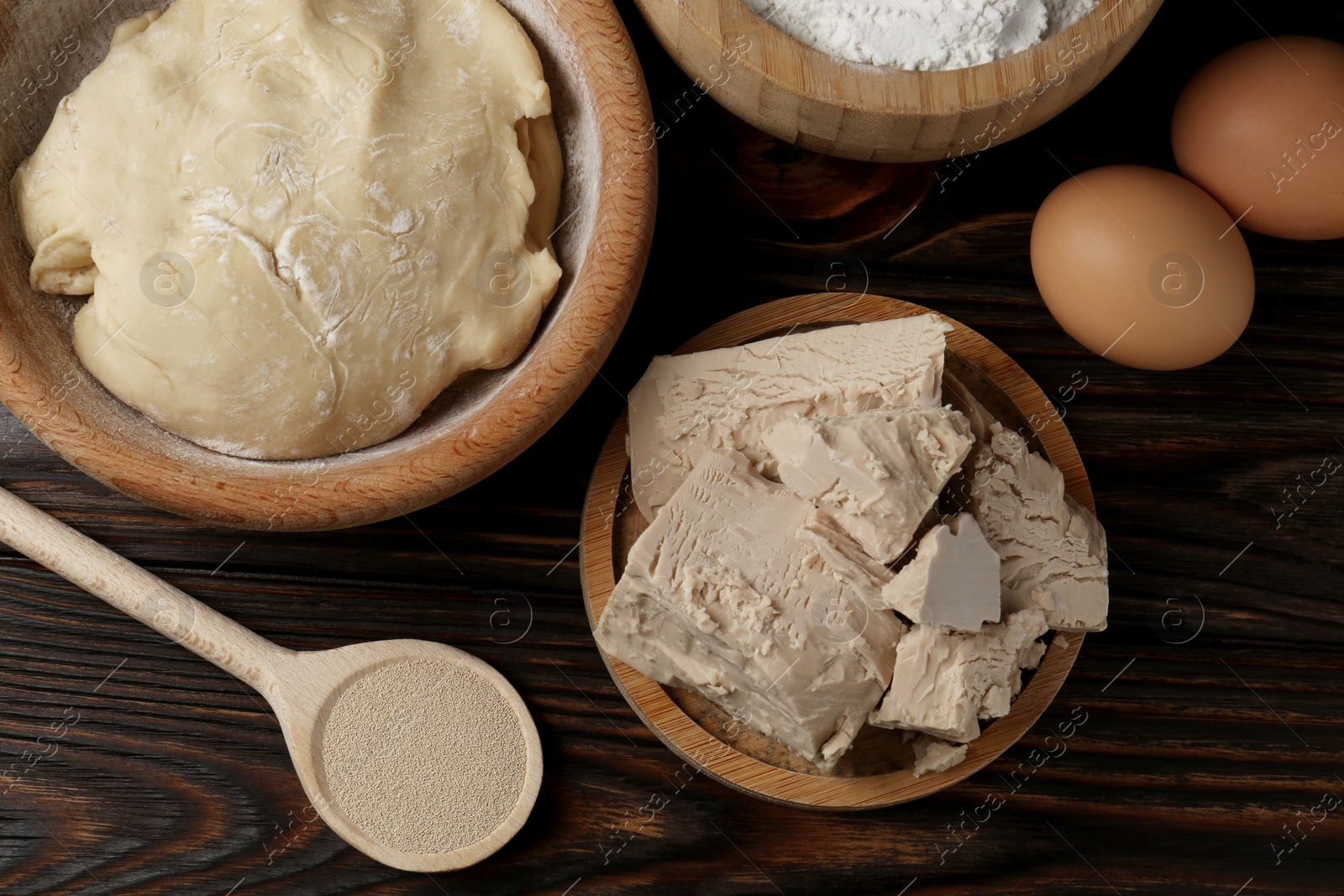 Photo of Different types of yeast, eggs, flour and dough on wooden table, flat lay