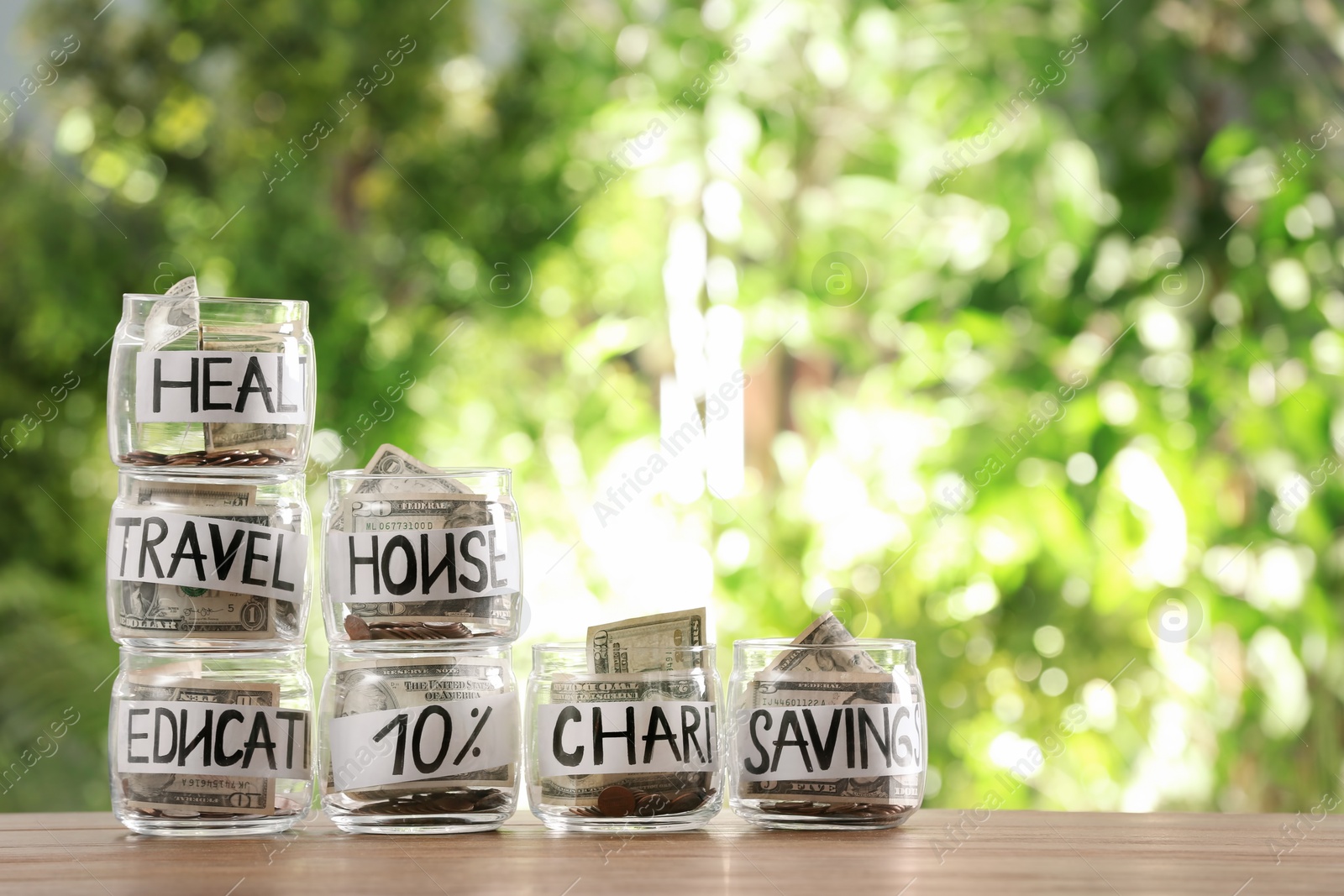 Photo of Glass jars with money for different needs on table against blurred background, space for text