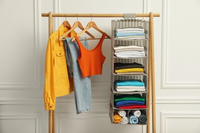 Wardrobe organization. Rack with different stylish clothes near white wall