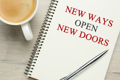 Image of Phrase New Ways Open New Doors and cup of coffee on white wooden table, flat lay