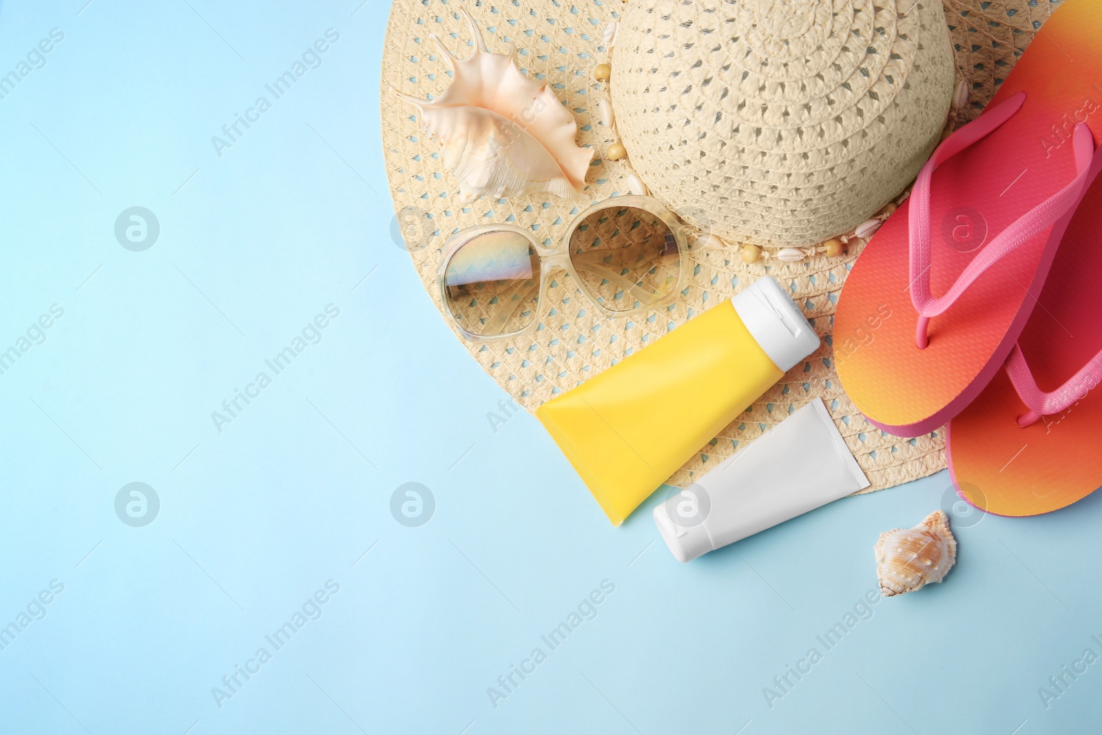 Photo of Flat lay composition with sunscreen and beach accessories on light blue background, space for text