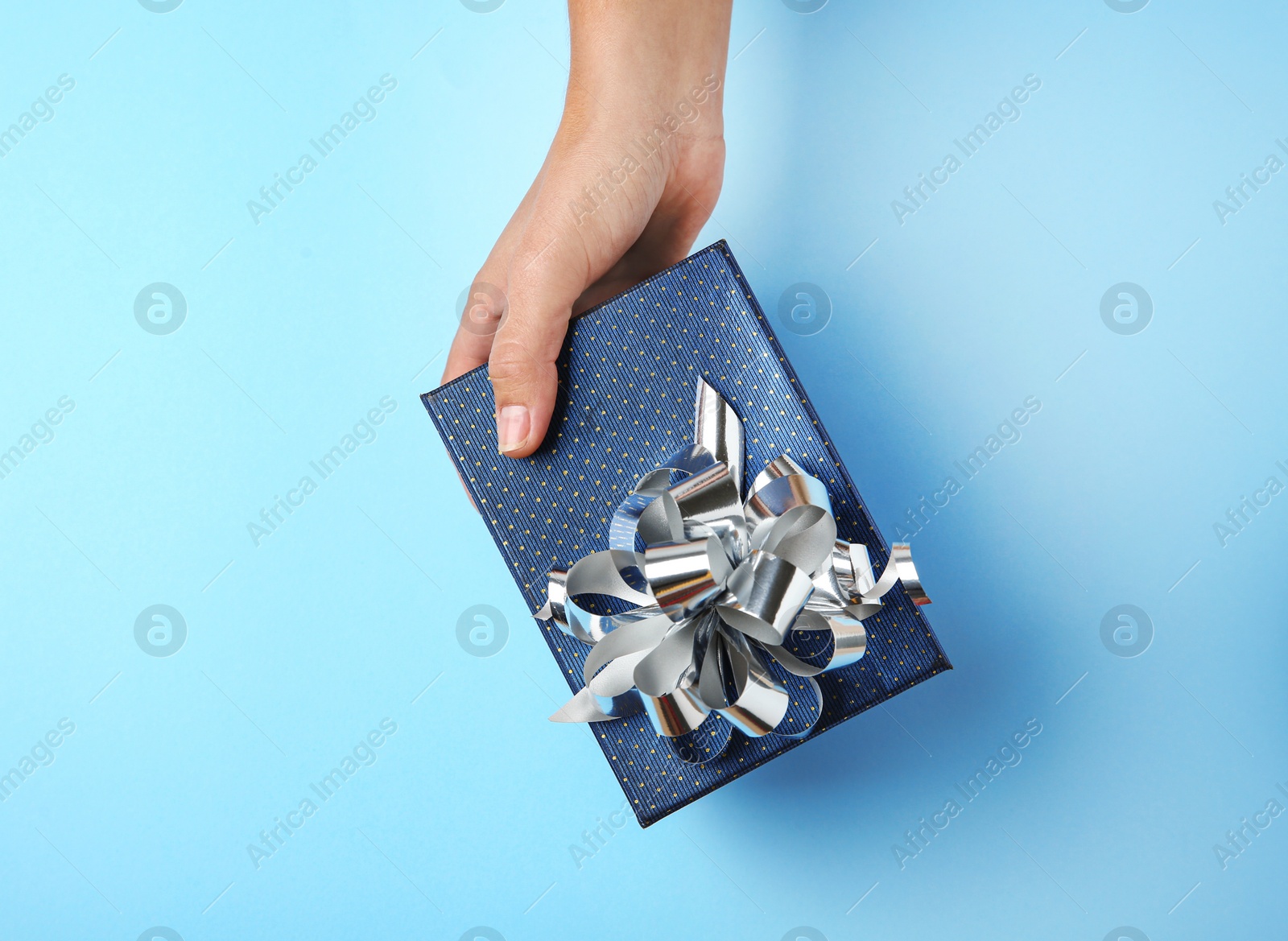 Photo of Woman holding beautiful gift box on blue background, top view