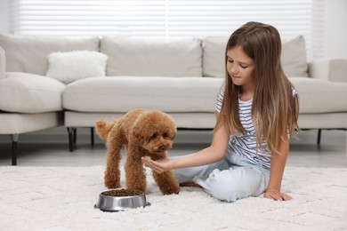 Photo of Little child feeding cute puppy on carpet at home. Lovely pet