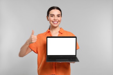 Photo of Happy woman with laptop showing thumb up on light gray background