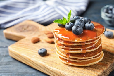 Photo of Wooden board with pancakes, syrup and blueberries on table, closeup