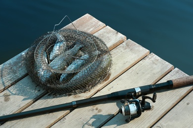 Photo of Fishing rod and fresh fish on wooden pier near pond