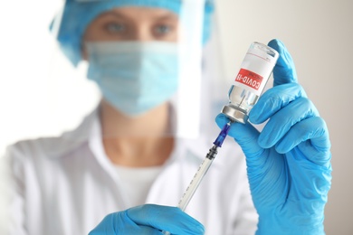 Photo of Doctor filling syringe with Covid-19 vaccine against light background, focus on hands. Space for text