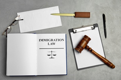 Photo of Flat lay composition with book, gavel and clipboard on grey background. Immigration law concept
