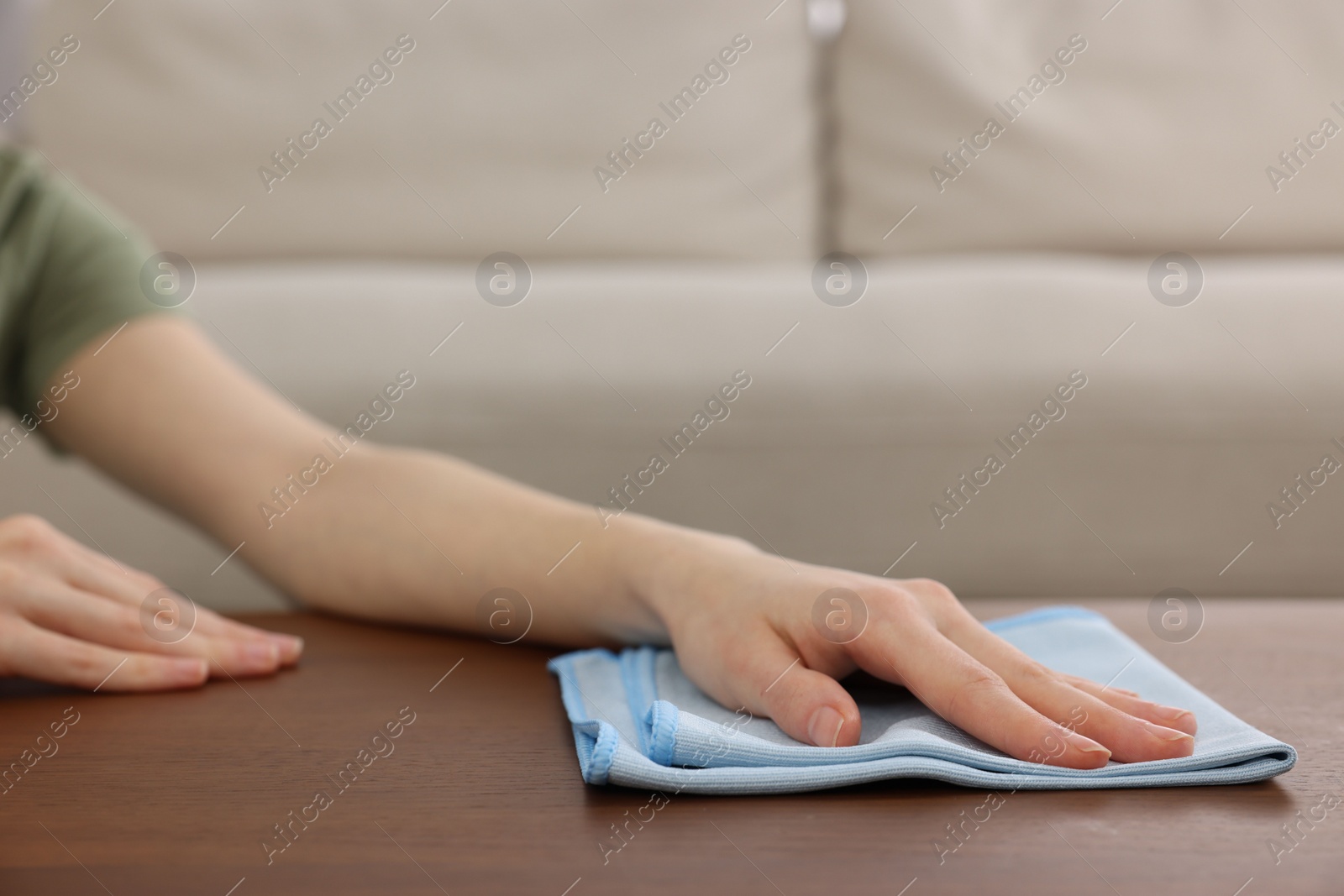 Photo of Woman with microfiber cloth cleaning wooden table in room, closeup. Space for text