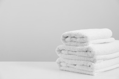 Photo of Stack of clean soft white towels on table against light grey background. Space for text