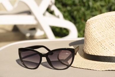 Photo of Stylish hat and sunglasses on grey sunbed outdoors, closeup