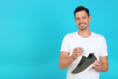 Photo of Man putting capsule shoe freshener in footwear on color background